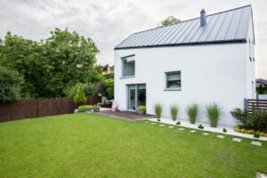 White house with windows and green garden with trees outside