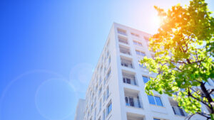 A modern residential building in the vicinity of trees. Ecology and green living in city, urban environment concept. Modern apartment building and green trees. Ecological housing architecture.